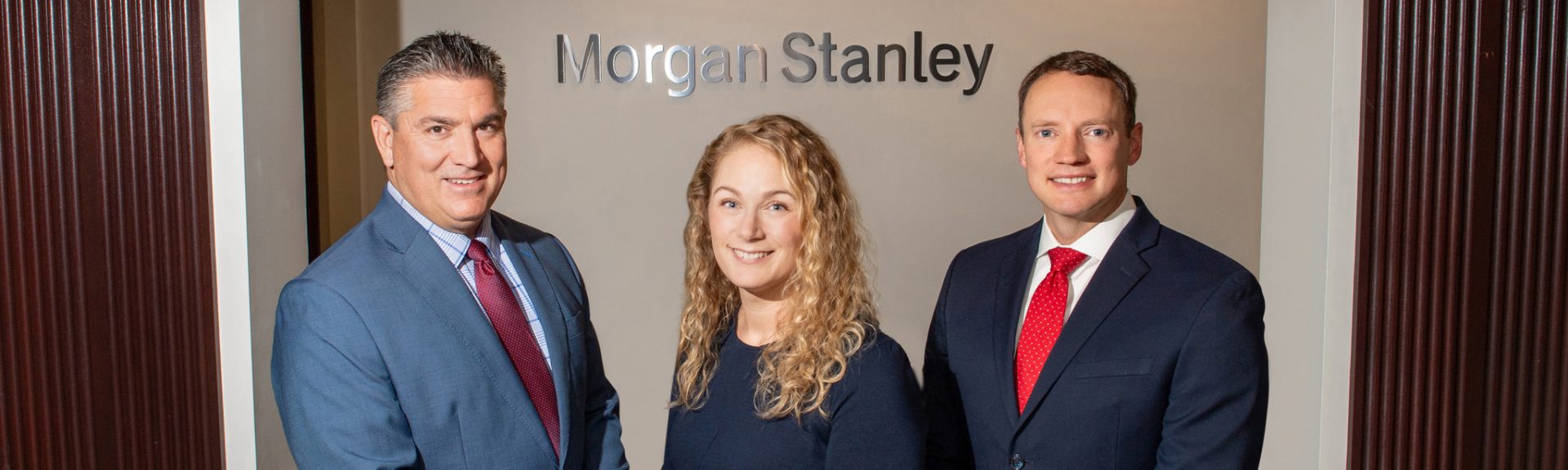 Three people in business attire stand in front of a wall with the Morgan Stanley logo.