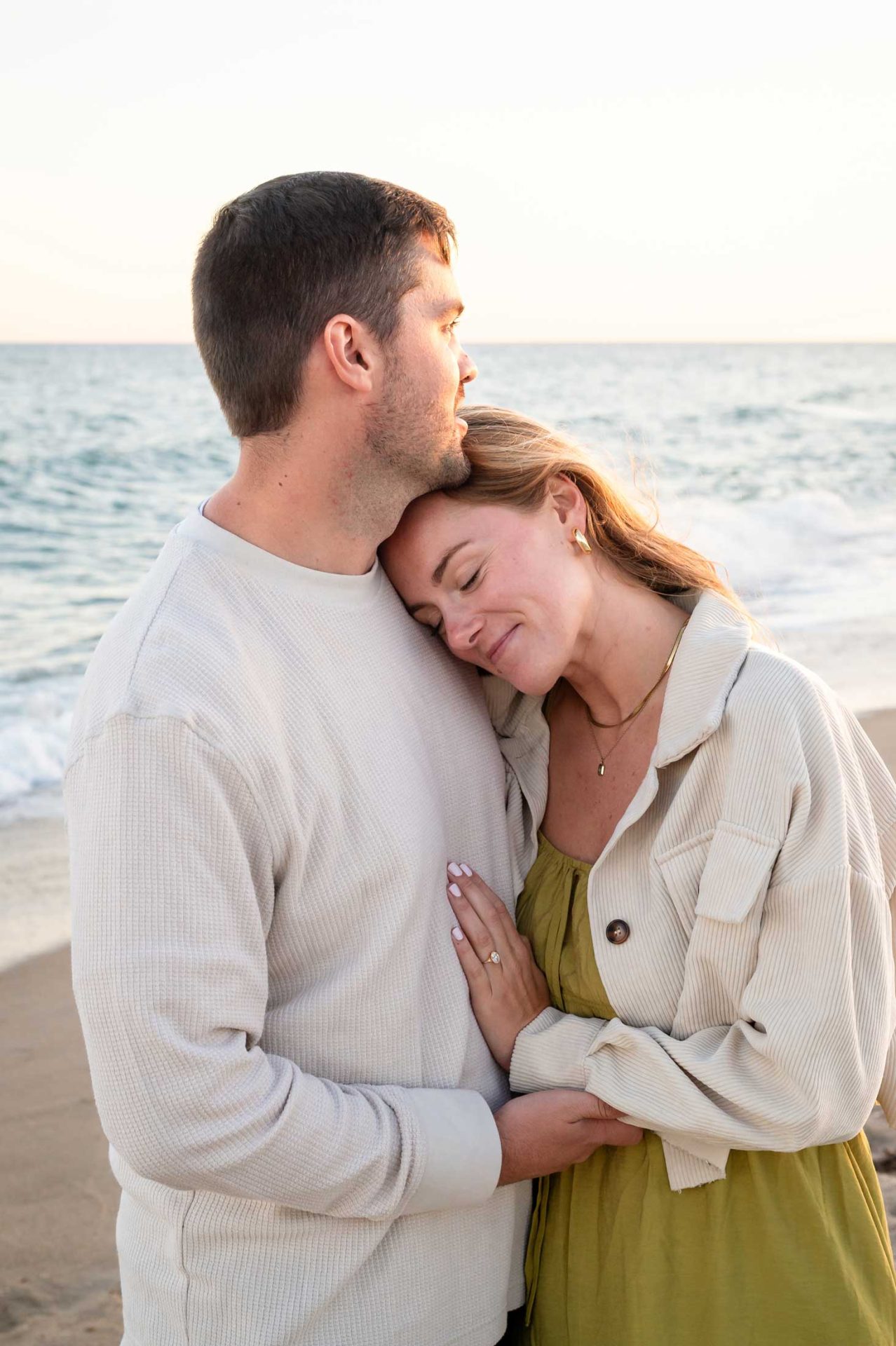 beach proposal A man and woman stand close together on a beach; the woman rests her head on the man’s chest while he looks out over the ocean.