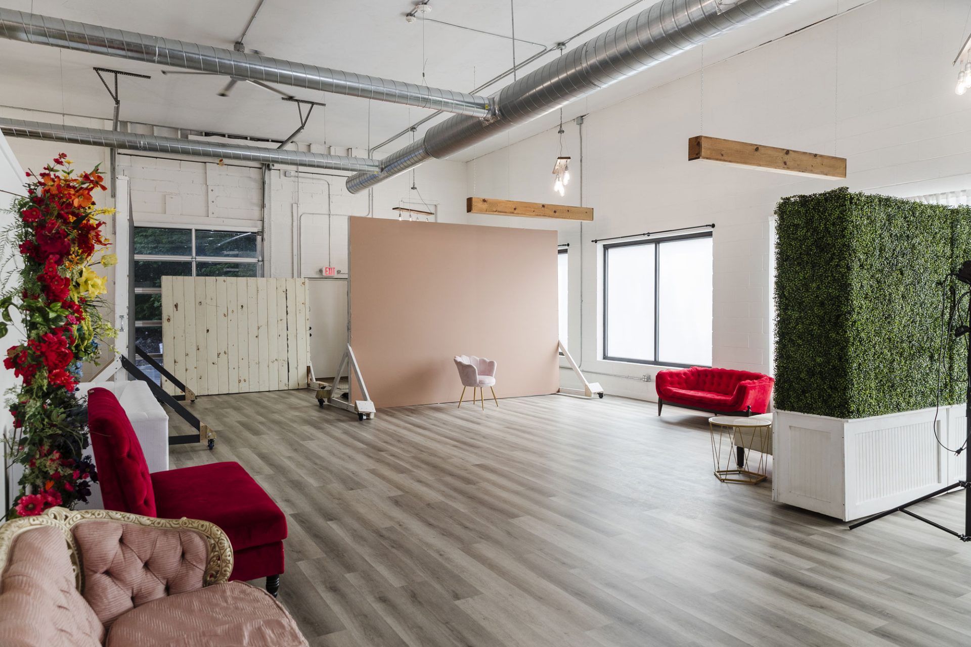 nicole-gesmondi-studio-pink-wall Large photo studio space with wood flooring, various couches, a pink backdrop, greenery divider, and natural light from big windows.