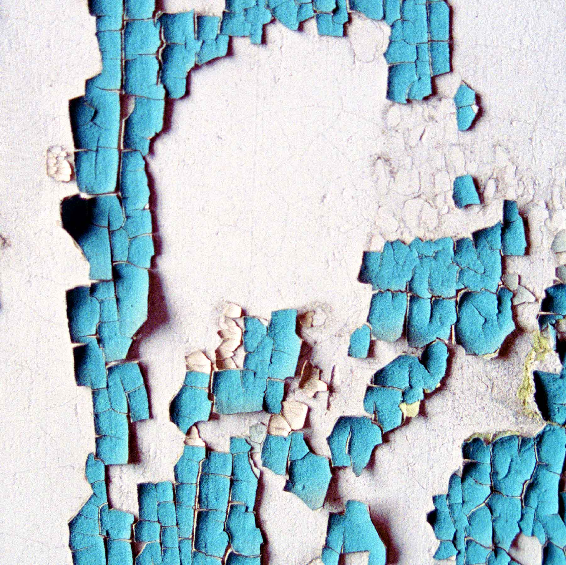 fine-art-photography-peeling-paint-Blue-Map Close-up of peeling blue paint on a white wall, showing cracked and chipped sections with exposed surface underneath.