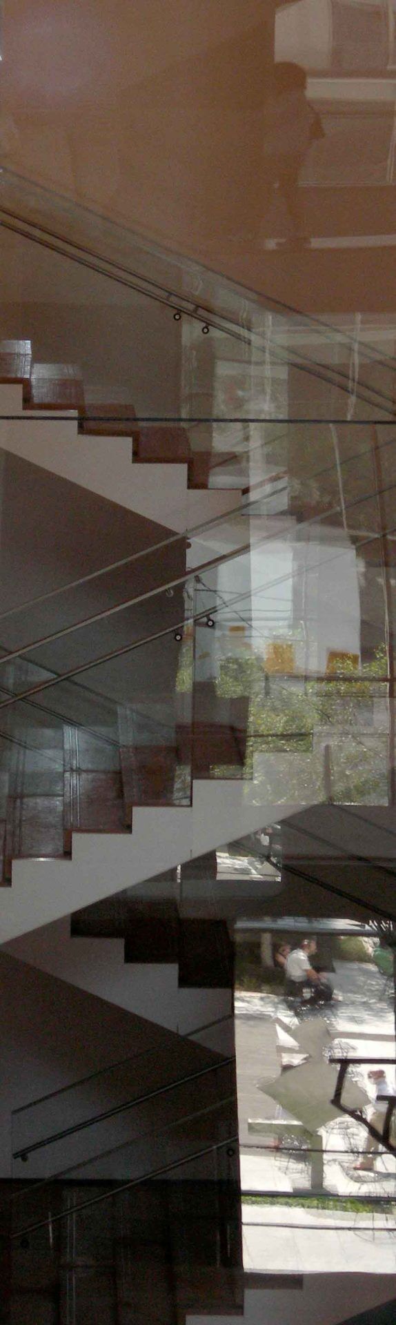 fine-art-photography-reflections-Dont-Stare A modern staircase with glass railings and wooden steps is reflected in a large window, showing an outdoor street scene with parked motorcycles.
