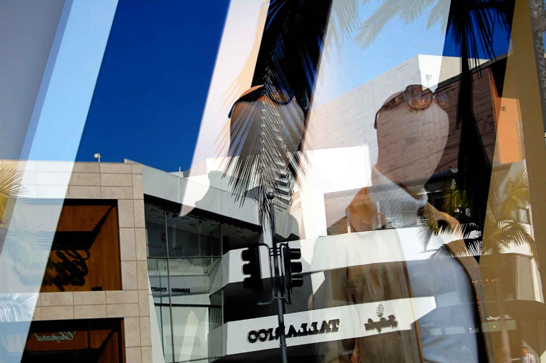 fine-art-photography-reflections-Rodeo-Reflections A city street scene with modern buildings, palm trees, and a traffic light, overlaid with reflections of mannequins in a shop window.