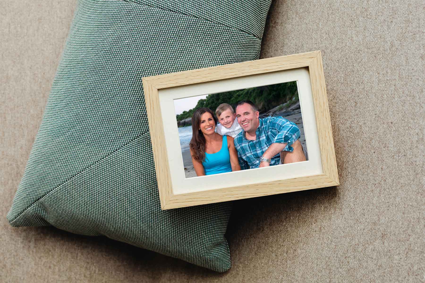 framed-beach-session-picture A framed photo of a smiling woman, child, and man sitting together outdoors, placed on a textured cushion.