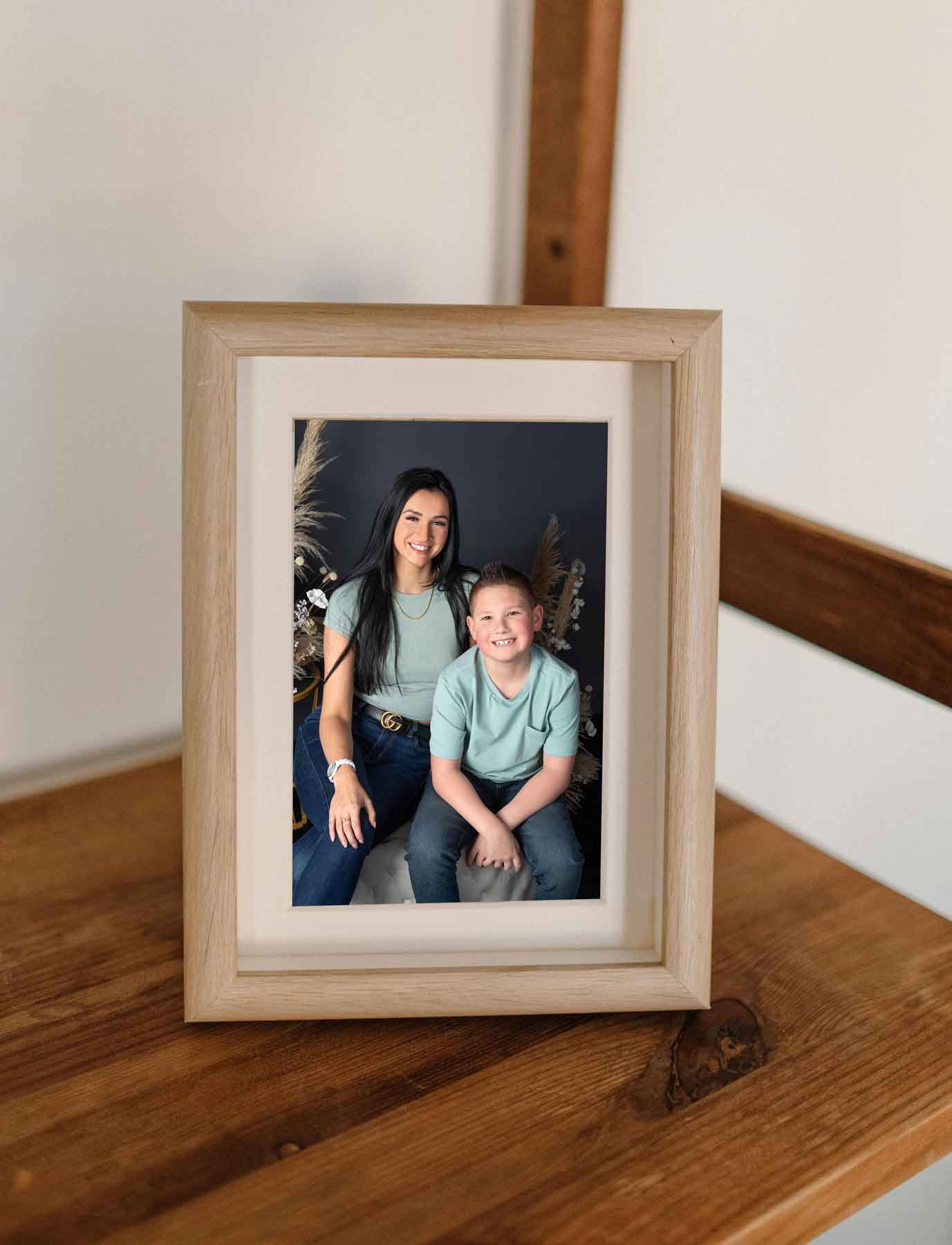 framed-mothers-day-picture A framed photo of a woman and a young boy sitting together and smiling, displayed on a wooden surface near a staircase railing.