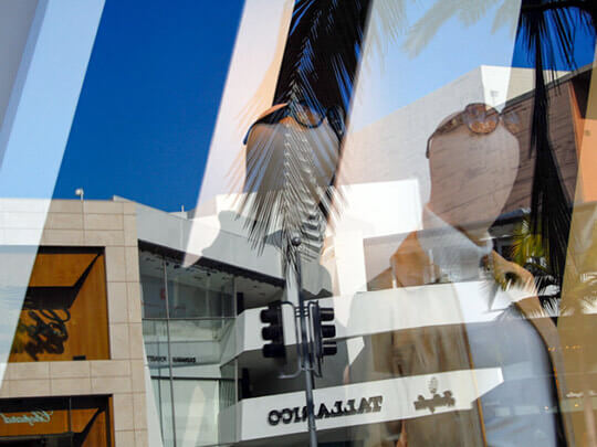 nicole gesmondi fine art photography Rodeo-Reflections Storefront mannequins and palm tree reflections overlapping with modern shopping mall architecture under a clear blue sky.