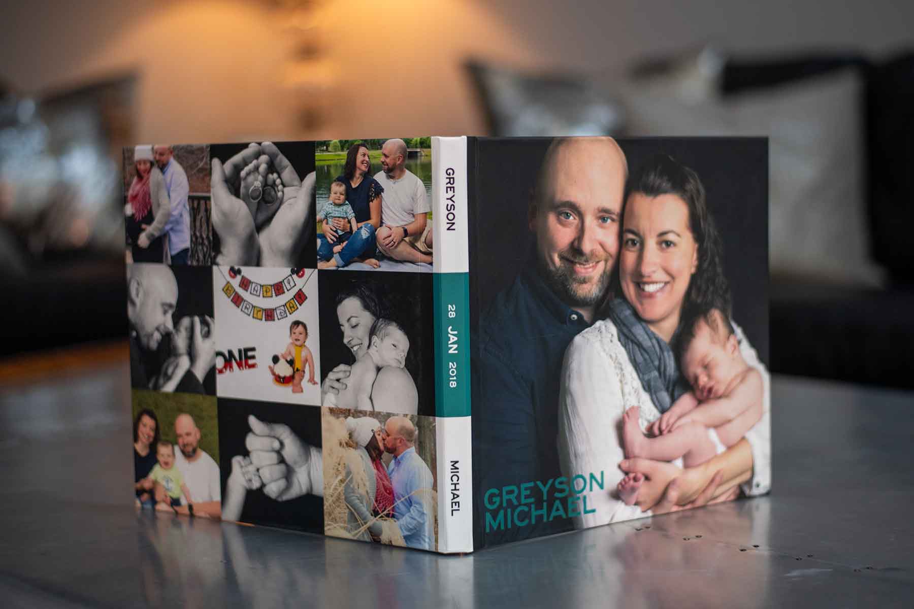 A photo book with family photos on the cover, featuring a couple holding a baby and the name “Greyson Michael” with the date “28 Jan 2018” on the spine.