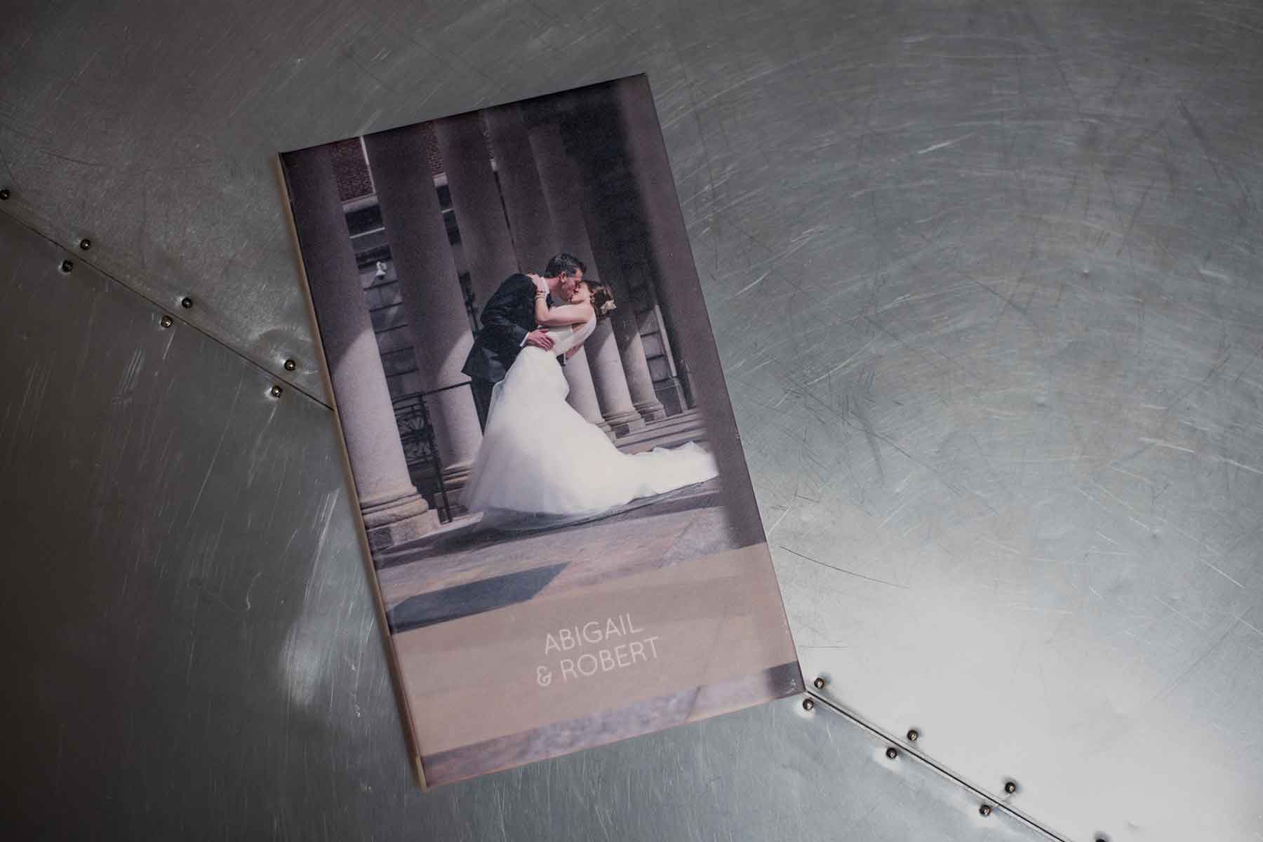 A wedding photo booklet titled "Abigail & Robert" lies on a metallic, riveted surface.