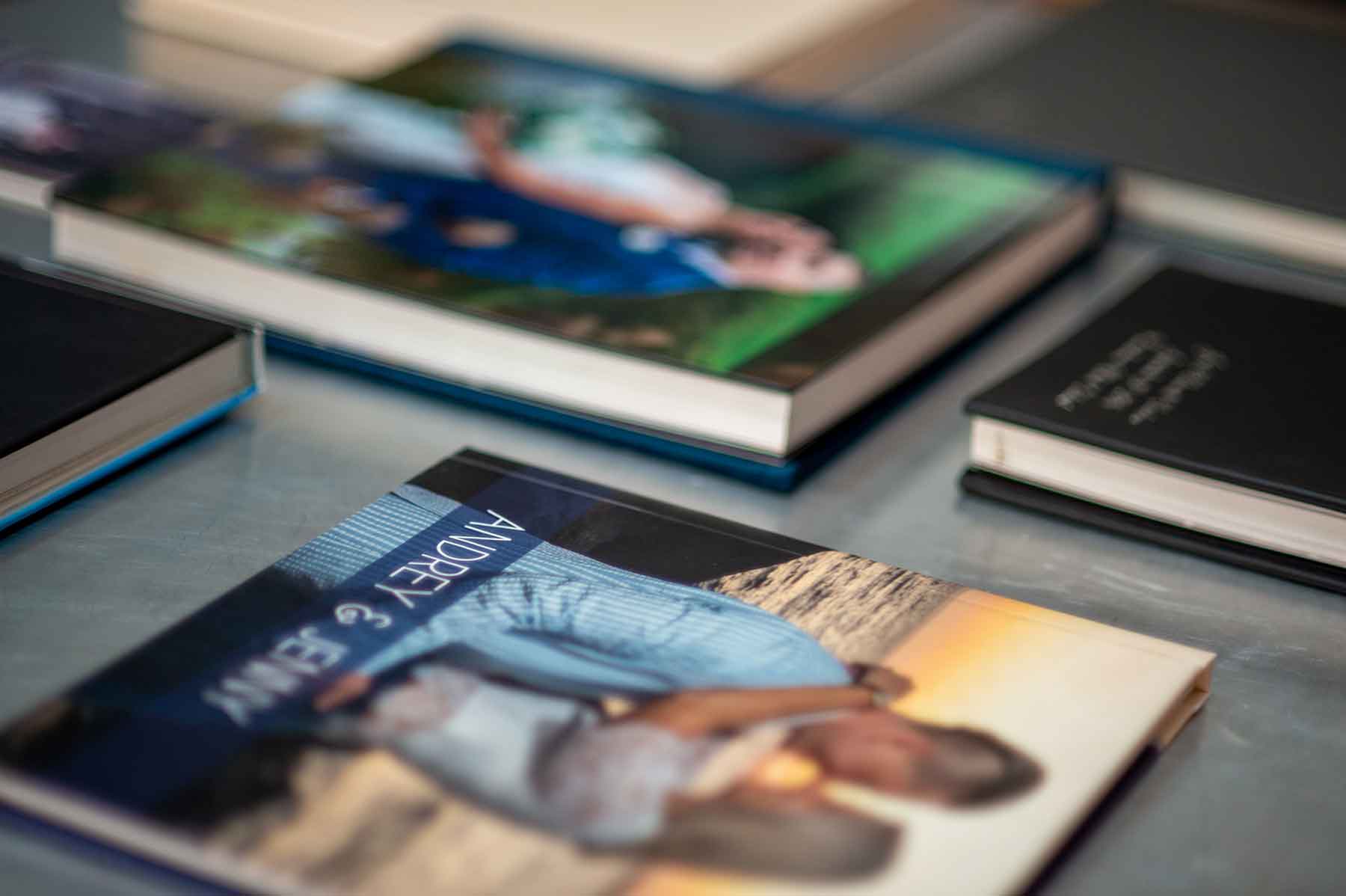 Several hardcover photo books are displayed on a table, with one prominently showing a cover image of a couple embracing at sunset.