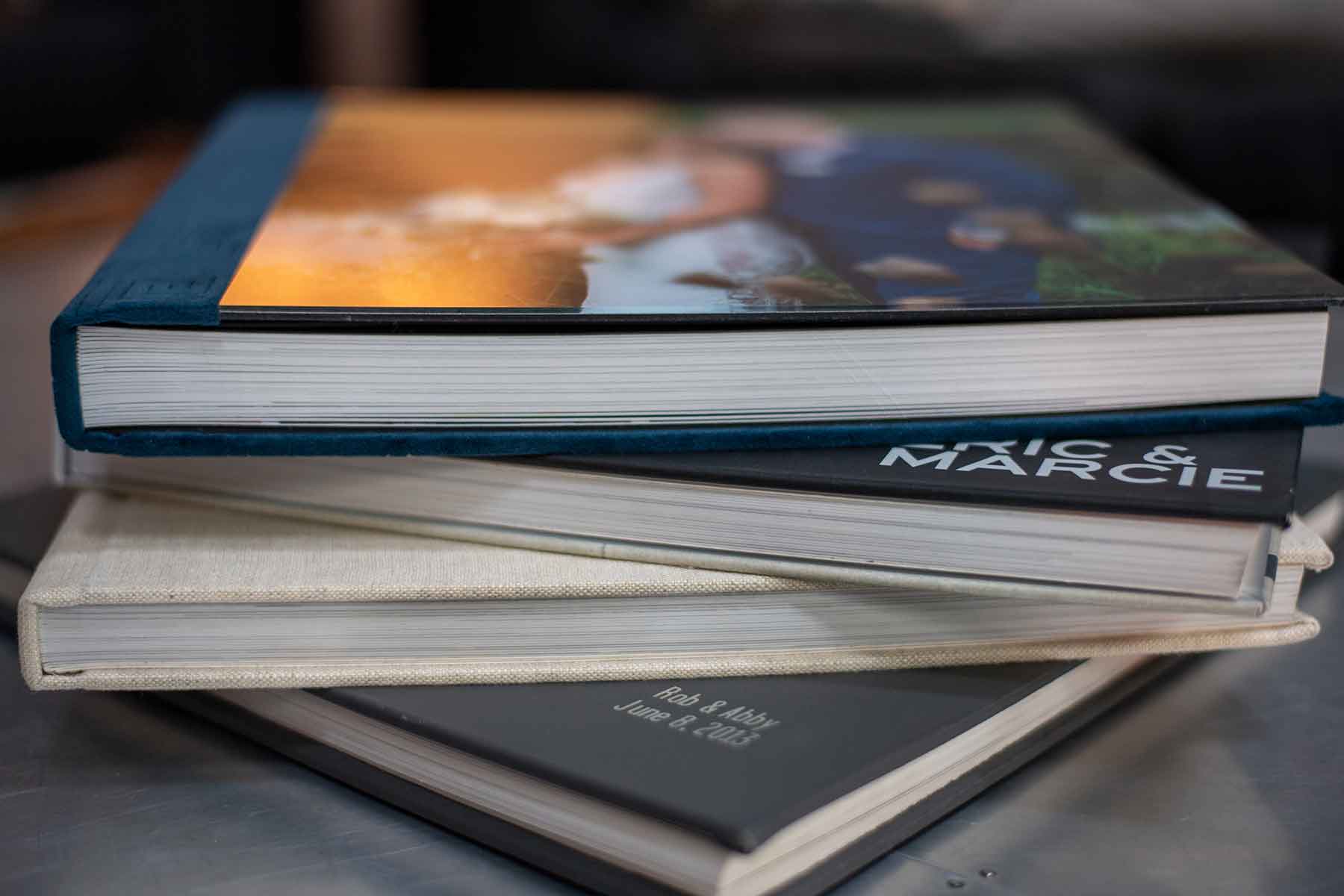 A close-up of three stacked photo albums with personalized covers, showing thick pages and partially visible names and dates on the spines.