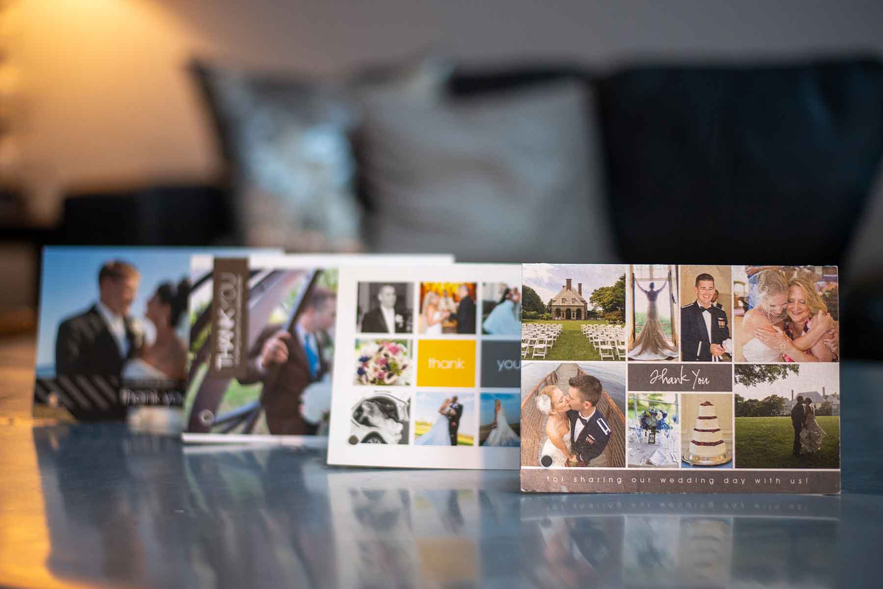 Four thank you cards featuring wedding photos are displayed upright on a reflective surface with a blurred couch and pillows in the background.