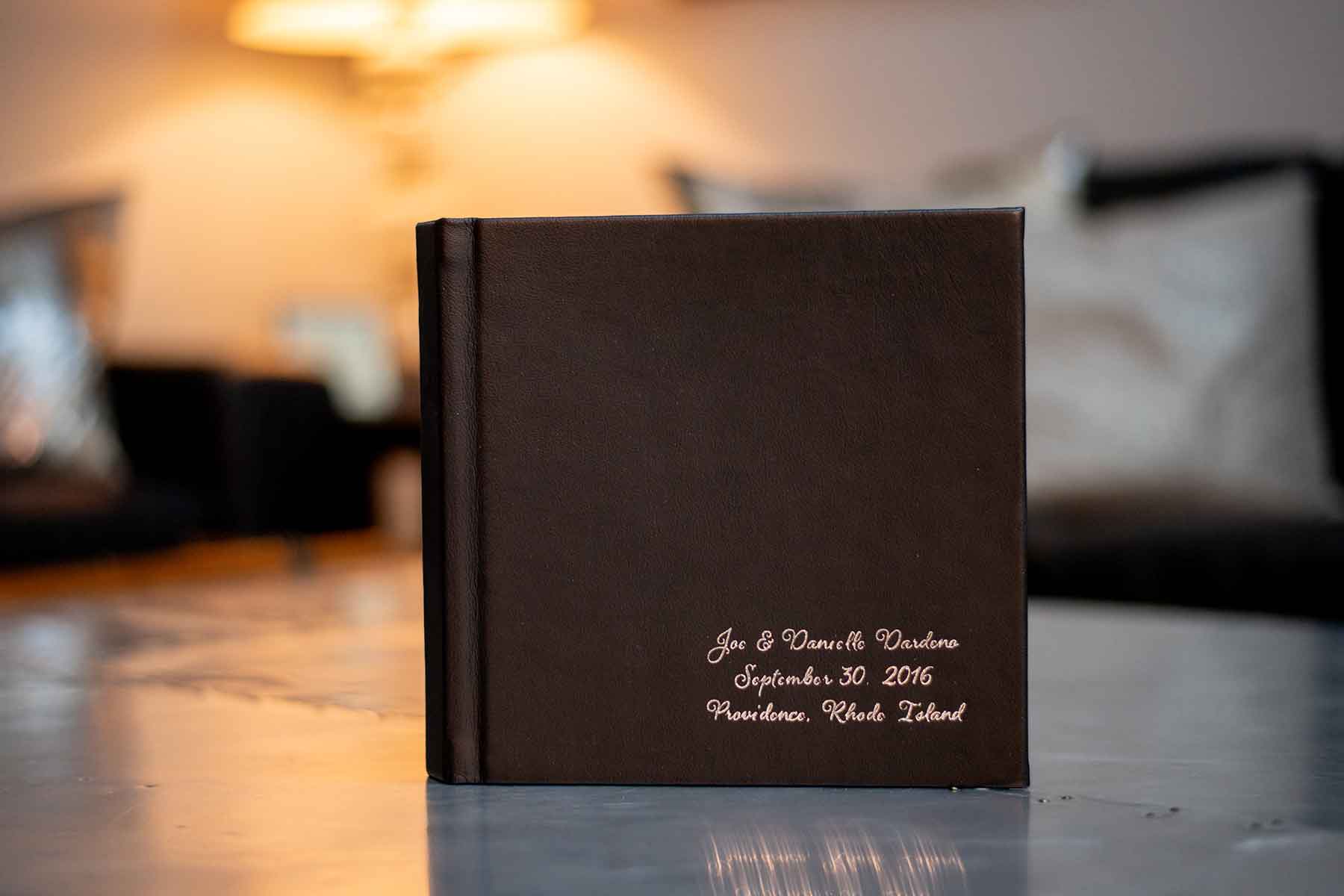A brown photo album with white text reading "Joe & Danielle Vardaro, September 30, 2016, Providence, Rhode Island," resting on a table in a softly lit room.