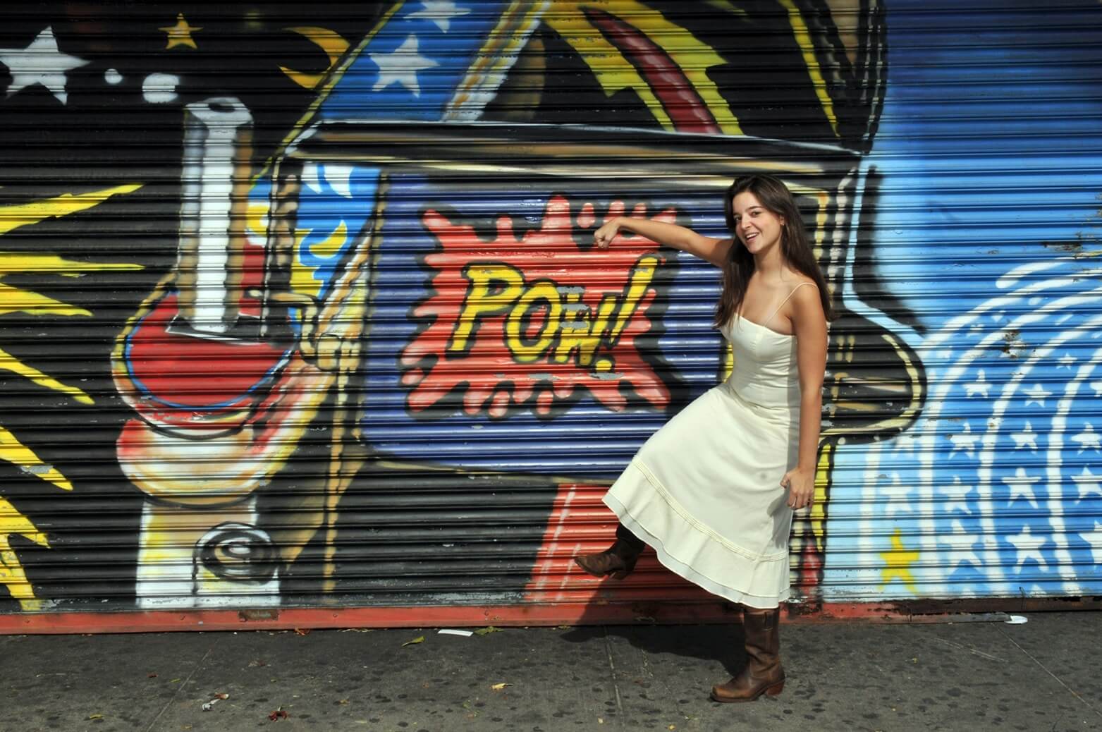 ri-trash-the-dress-photographer-016 Woman in a white dress and brown boots poses in front of a colorful mural featuring the word "POW!" in comic book style.