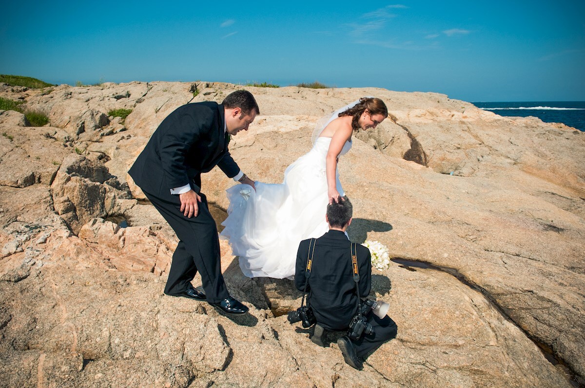 Paul helping Kate on the rocks Photographer helping bride and groom on the rocks
